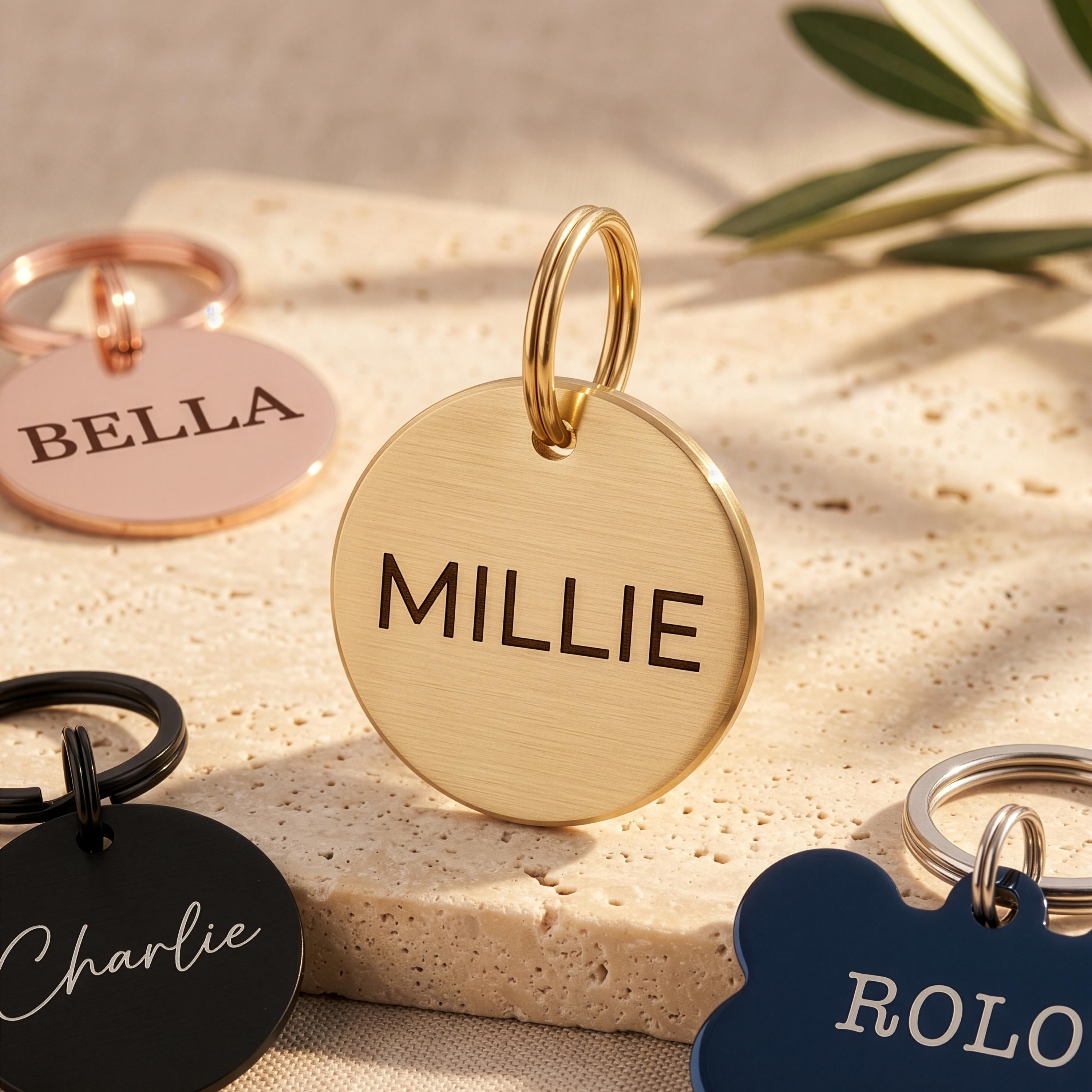Gold personalised dog tag engraved MILLIE, with rose gold, black and blue tags from the range around it
