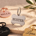 Silver bone dog tag engraved BUSTER in brushed stainless steel, with rose gold, black and gold tags around it