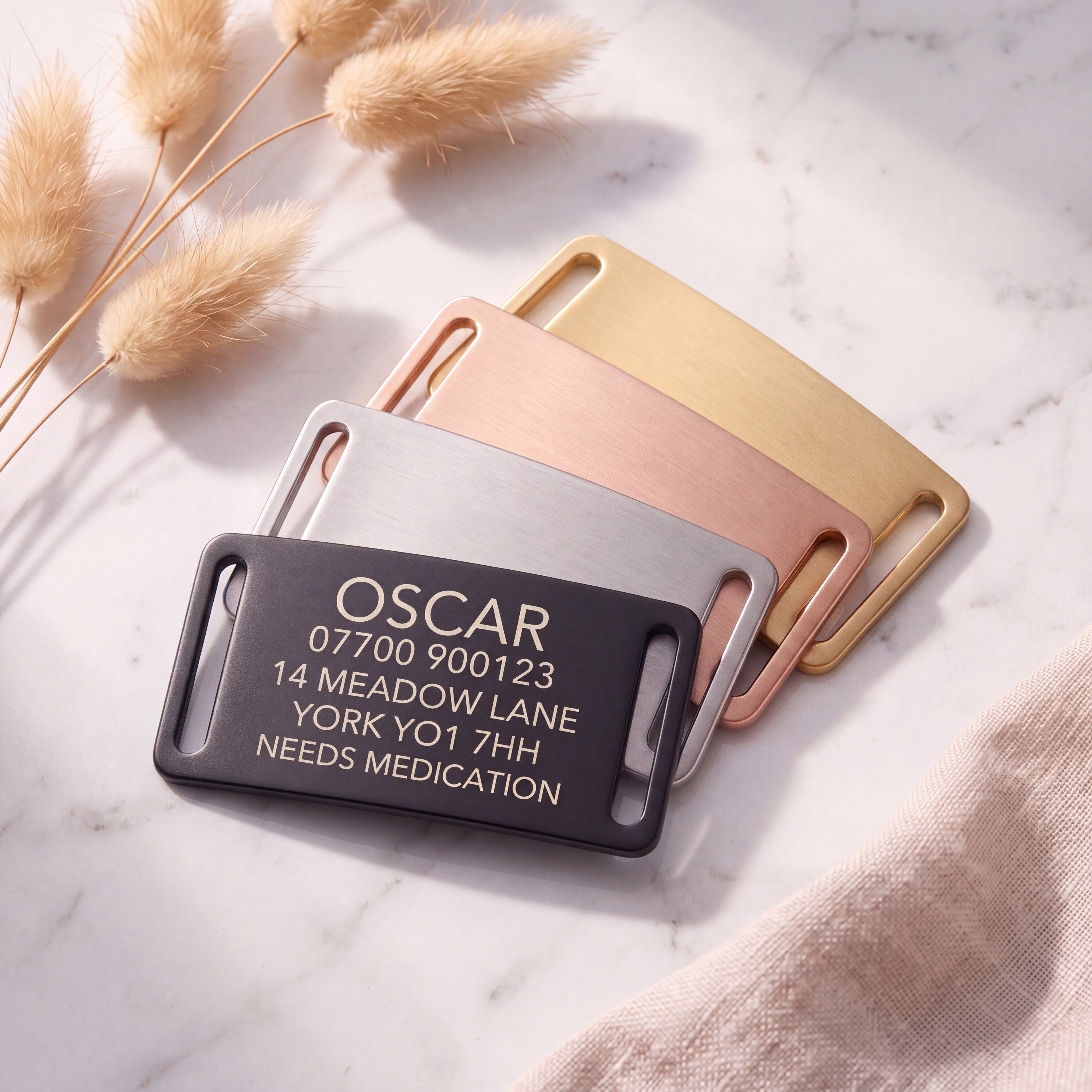 Personalised black slide-on dog tag leading a fanned set of all four brushed finishes on marble