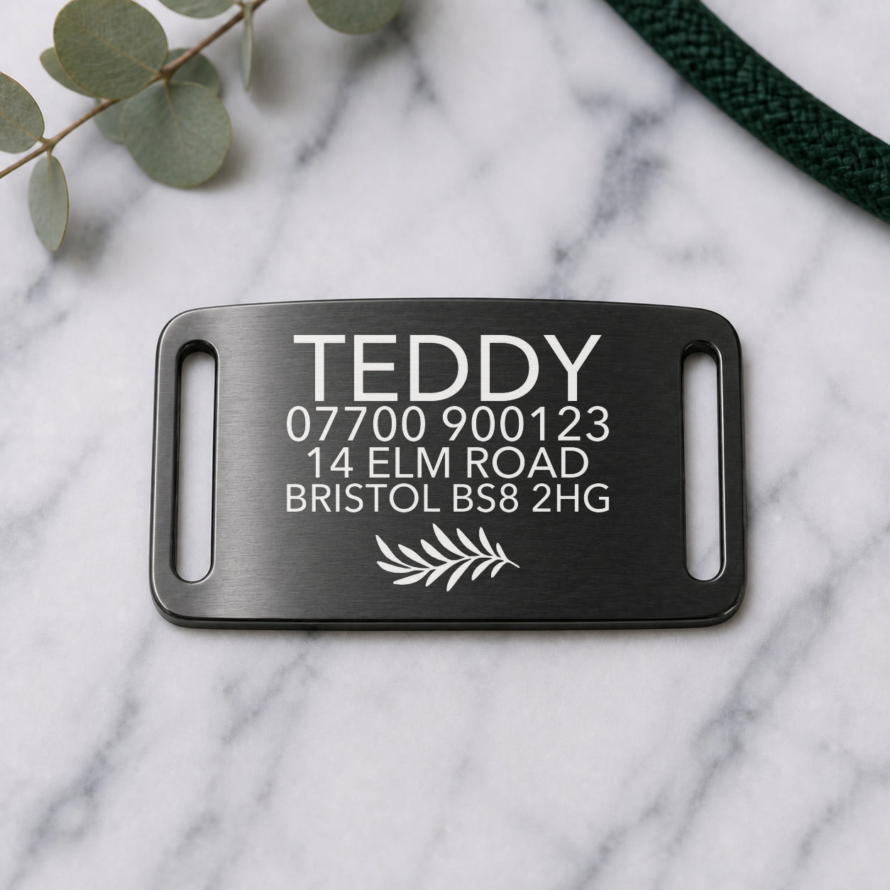 Brushed black slide-on dog tag engraved with a name, styled on marble