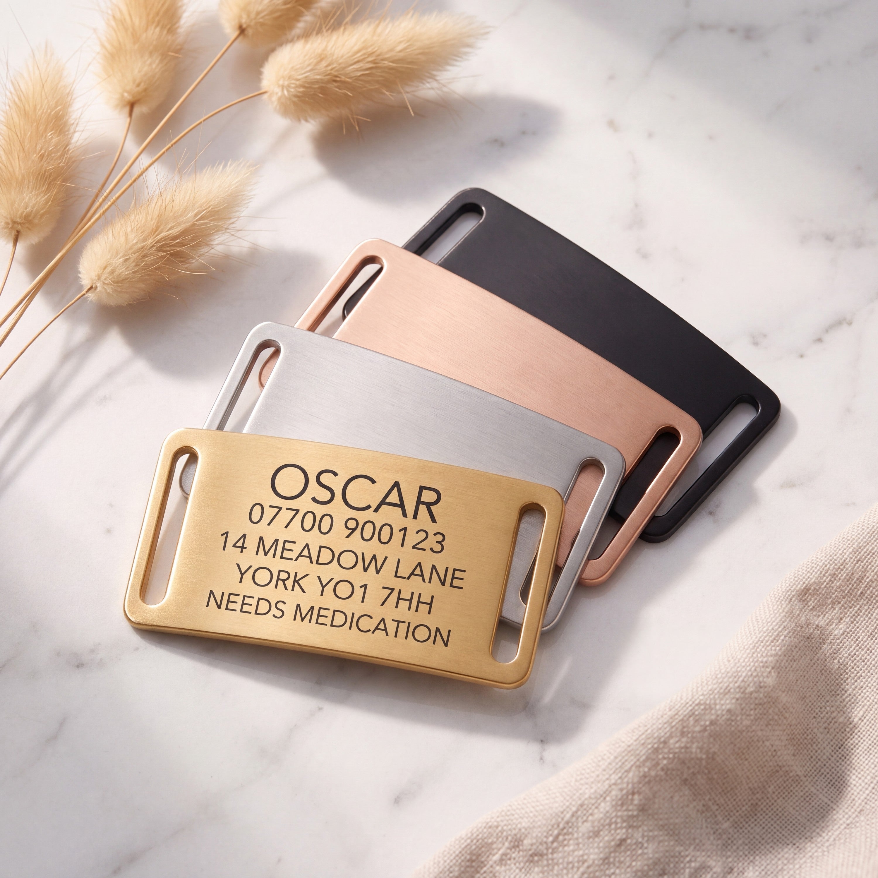 Personalised gold slide-on dog tag leading a fanned set of all four brushed finishes on marble