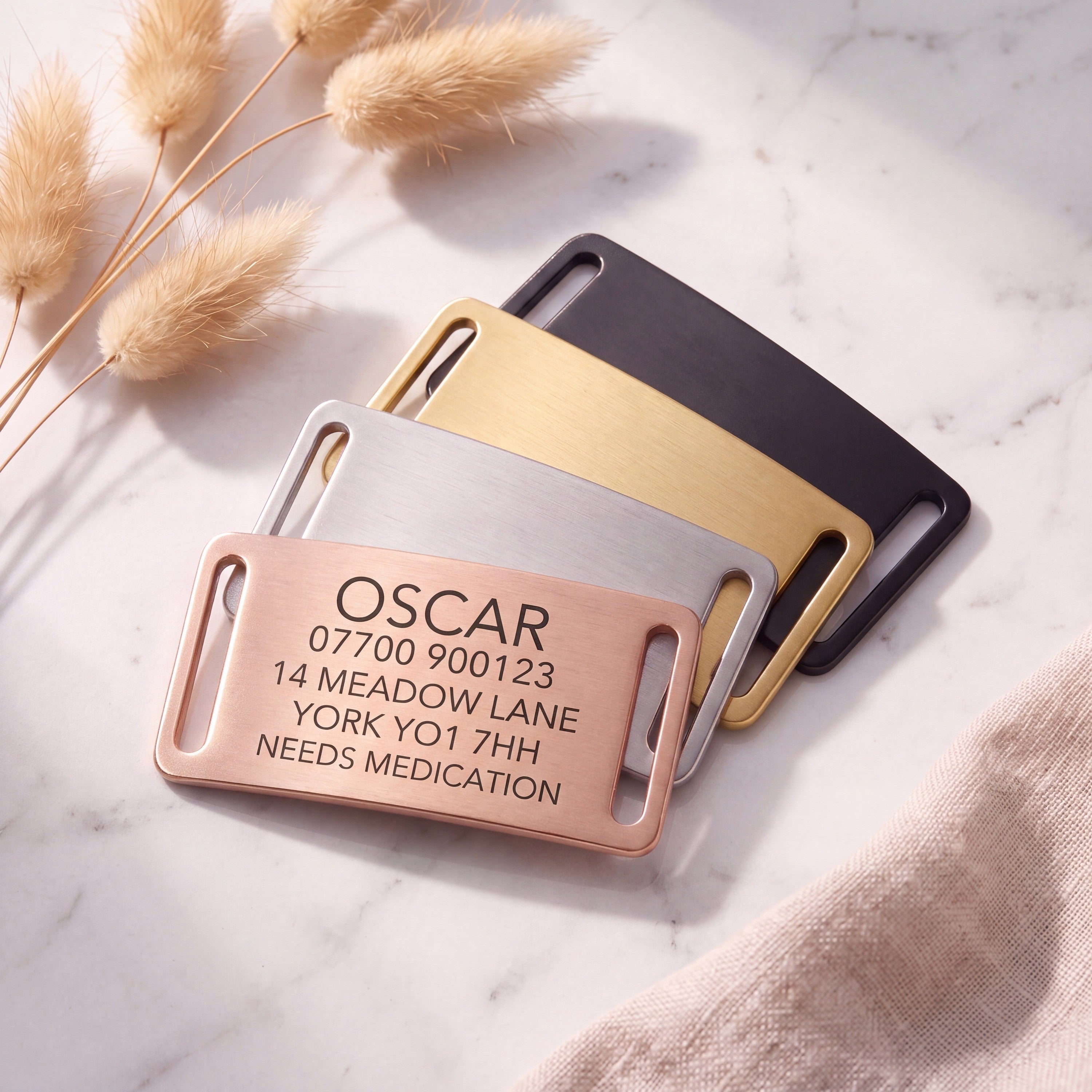 Personalised rose gold slide-on dog tag leading a fanned set of all four brushed finishes on marble