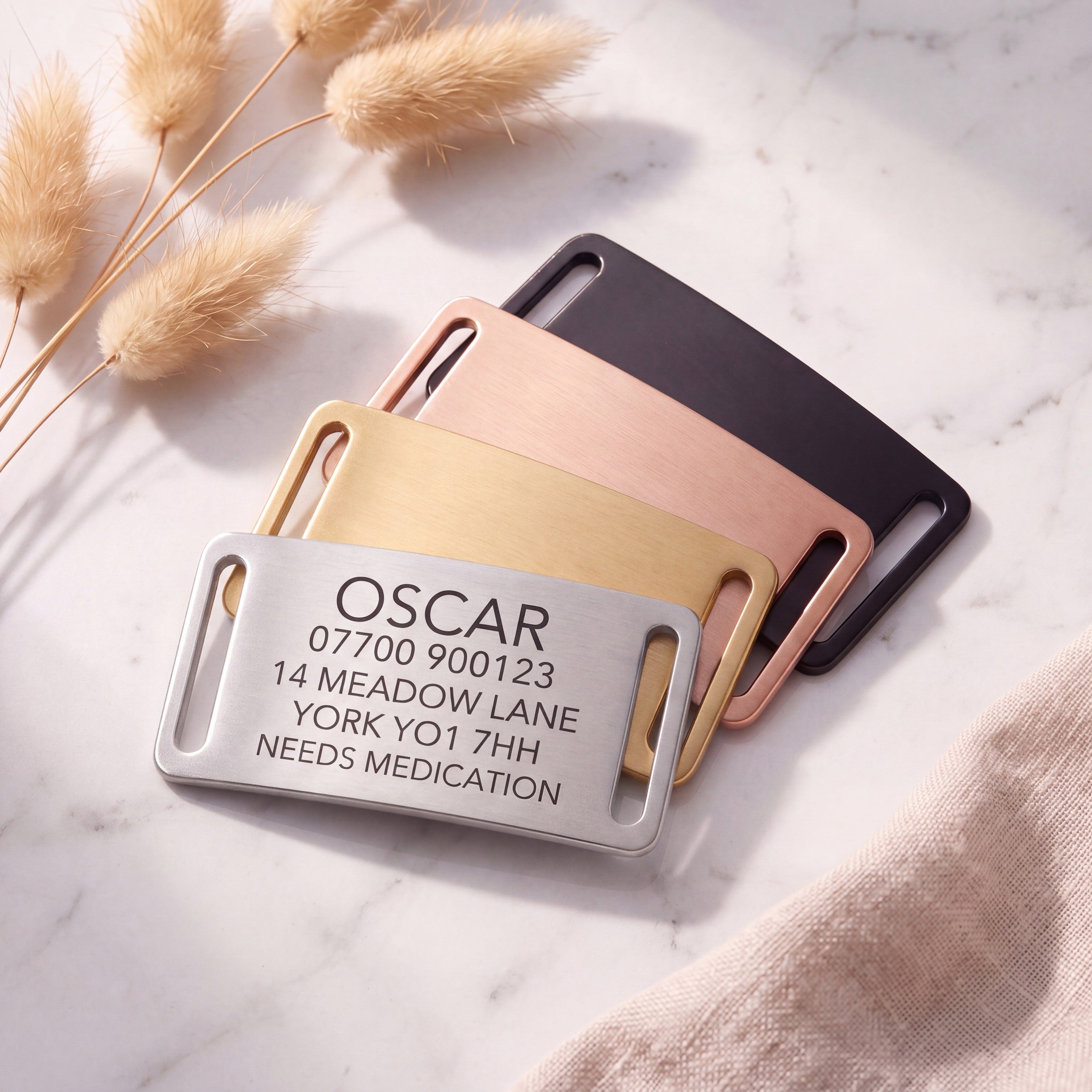 Personalised silver slide-on dog tag leading a fanned set of all four brushed finishes on marble